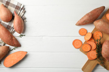 Sweet potato, board and towel on white wooden background, top view
