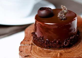 Chocolate cake stands on a decorative wooden plate next to a white cup of coffee