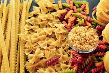 Italian raw pasta, types of pasta. Light background, top view, close-up. Farfalle, fettuccine, fusilli, colored pasta, tagliatelle.