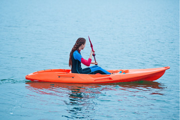 Obraz premium Kayaking. Girl on an orange kayak swims on the lake