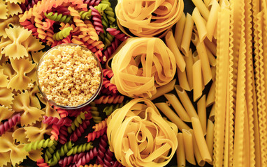 Italian raw pasta, types of pasta. Light background, top view, close-up. Farfalle, fettuccine, fusilli, colored pasta, rotini, tagliatelle, tripolini, anellini.