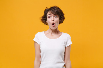 Shocked young brunette woman girl in white t-shirt posing isolated on yellow orange wall background studio portrait. People sincere emotions lifestyle concept. Mock up copy space. Keeping mouth open.
