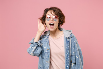 Curious young brunette woman girl in casual denim jacket, eyeglasses posing isolated on pastel pink...