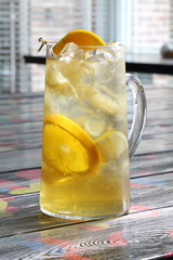 Glass jug with lemonade from oranges and lemons on a wooden table