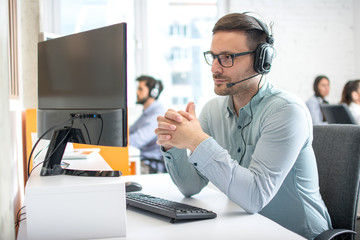 Customer service support operator man with headphones and microphone listening to his client in call center - obrazy, fototapety, plakaty