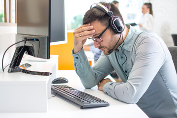 Call center operator man wearing headset suffering from headache at office
