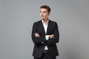 Obraz na płótnie Canvas Successful young business man in classic black suit shirt posing isolated on grey wall background. Achievement career wealth business concept. Mock up copy space. Holding hands crossed, looking aside.