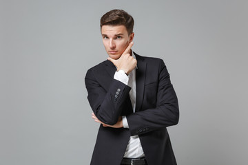 Confident young business man in classic black suit shirt posing isolated on grey background studio portrait. Achievement career wealth business concept. Mock up copy space. Put hand prop up on chin.