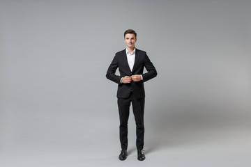 Fototapeta na wymiar Confident young business man in classic black suit shirt posing isolated on grey background studio portrait. Achievement career wealth business concept. Mock up copy space. Fastening button on jacket.