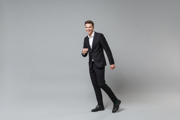 Fototapeta na wymiar Side view of laughing young business man in classic black suit shirt posing isolated on grey wall background in studio. Achievement career wealth business concept. Mock up copy space. Looking camera.