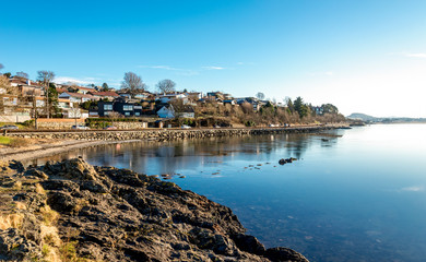Fototapeta na wymiar Scenic coastal view of Hafrsfjord bay covered by thin ice and residential houses of the suburb near Sword in Rock monument, Stavanger, Norway, February 2018