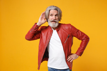 Curious elderly gray-haired mustache bearded man in red leather jacket posing isolated on yellow...