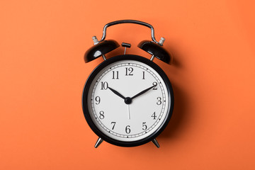 Black vintage alarm clock on orange background. Time concept