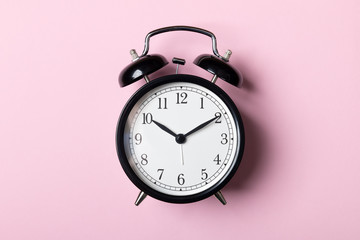 Black vintage alarm clock on pink background. Time concept
