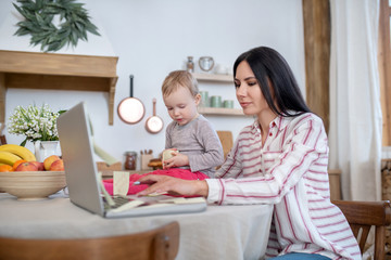 Young mom typing on laptop, daughter sitting next to her