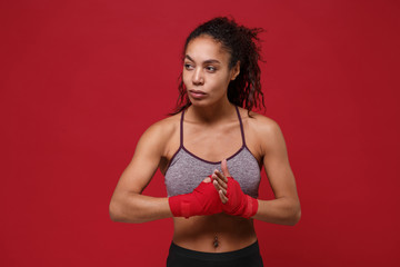 Beautiful young african american sports fitness boxer woman in sportswear posing working out isolated on red background. Sport exercise healthy lifestyle concept. Wearing sports bandages on her hands.