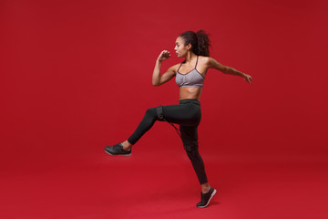 Side view of young african american sports fitness woman in sportswear working out isolated on red background in studio. Sport exercises healthy lifestyle concept. Doing exercises with elastic band.