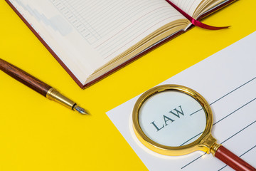 Office still life yellow table with notebook, gilded pen and Law on which a magnifying glass is preparing for the notes