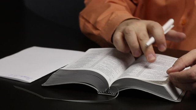 A man reads the Bible while sitting at the table. Writes important thoughts on a piece of paper. Corrects a bookmark and closes the book. Close-up shot