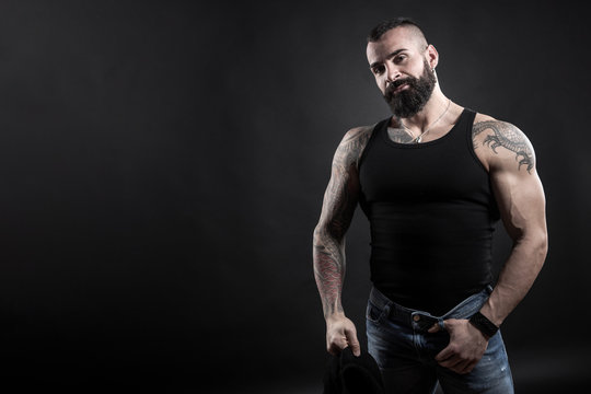 Uomo tatuato con canotta e jeans, isolato su sfondo nero