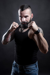 Uomo con barba e tatuaggi in posizione di lotta , isolato su sfondo nero