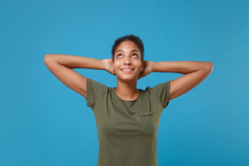 Pensive young african american woman girl in casual t-shirt posing isolated on blue background studio portrait. People emotion lifestyle concept. Mock up copy space. Looking up with hands behind head.