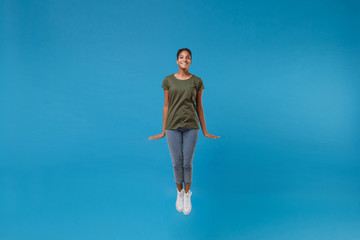 Fototapeta na wymiar Smiling young african american woman girl in casual clothes posing isolated on bright blue background studio portrait. People emotions lifestyle concept. Mock up copy space. Jumping, spreading hands.