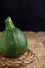 Close-up of a round zucchini on rustic wooden board, vertical black background with copy space