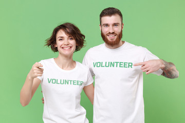 Smiling two young friends couple in white volunteer t-shirt isolated on green background. Voluntary...