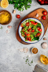 Fresh vegetable salad with dressing of mustard, olive oil, garlic, lemon and herbs in a plate on a gray concrete background, top view, copy space. Healthy mediterranean cuisine, vegetarian food