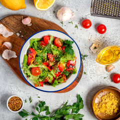 Fresh vegetable salad with dressing of mustard, olive oil, garlic, lemon and herbs in a plate on a gray concrete background, top view. Healthy mediterranean cuisine, vegetarian food, flat lay