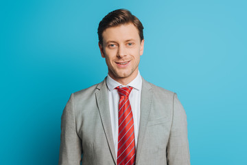 handsome businessman in grey suit smiling at camera on blue background