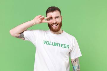 Cheerful young bearded man in white volunteer t-shirt isolated on pastel green background studio...
