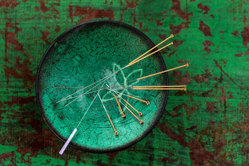 green ceramic Asian Bowl with needles for acupuncture on an old green paint wooden background - obrazy, fototapety, plakaty
