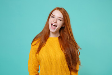 Cheerful funny young redhead woman girl in yellow sweater posing isolated on blue turquoise wall background studio portrait. People sincere emotions lifestyle concept. Mock up copy space. Blinking.