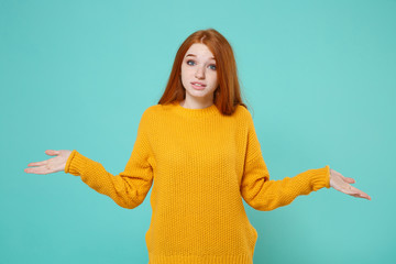 Perplexed young redhead woman girl in yellow sweater posing isolated on blue turquoise wall...