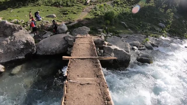 Trekker crossing log bridge in Pakistan mountains