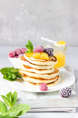Homemade pancakes with jam, frozen raspberries and blackberries and mint on wooden cutting board. Light grey background. Breakfast. 