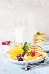 Pancakes with orange jam, frozen berries (raspberries and blackberries), mint and glass with milk on light blue stone background. Idea for children’s breakfast or snack. 