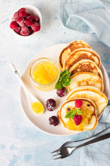 Pancakes with orange jam, frozen berries (raspberries and blackberries) and mint on light blue stone background. Breakfast. Top view. 
