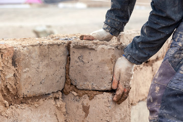 Close-up male hands build wall of unfinished house from clay brick
