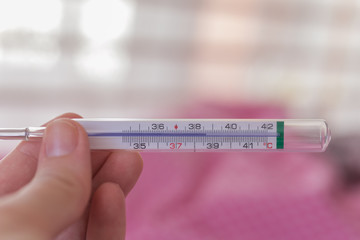 Close Up shot of a woman looking at thermometer. Female hands holding a thermometer showing high temperature. Shallow depth of field with focus on thermometer. Selected focus.