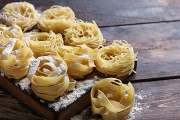 Concept of Italian cuisine. Dry pasta fettuccine and capellini with bowl with flour, eggs and wheat ears on an old wooden background. Background image, copy space