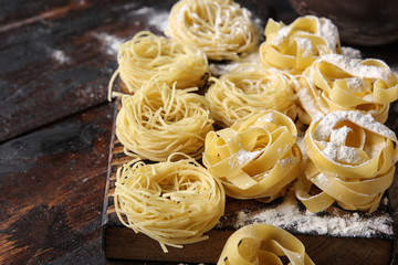 Concept of Italian cuisine. Dry pasta fettuccine and capellini with bowl with flour, eggs and wheat ears on an old wooden background. Background image, copy space