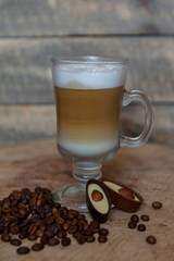 Latte coffee / cappuccino in a transparent glass with a pen on a wooden background. Coffee beans. Chocolate candies with nuts. Morning coffee concept.