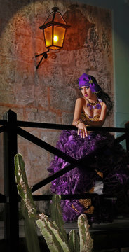 Joven recostada quinceañera en Cuba con vestido morado lila y gorro antiguo de la época. le acompañan, joyas, glamour y tradición.