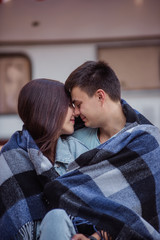 The newlyweds kiss covered in a blanket during their honeymoon trip near the trailer. Caring for each other.