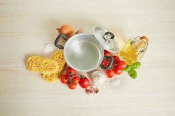 Ingredients for cooking - pasta, tomatoes, basilic, onions, olive oil on the bright wooden background. top view.
