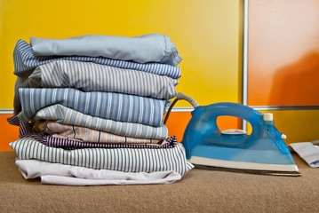 Stacked things on the ironing board. Iron and clothes on yellow and orange background.