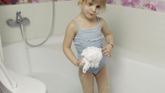 Cute blonde girl takes a bath in swimwear. Little child, 4 years old. Hygiene